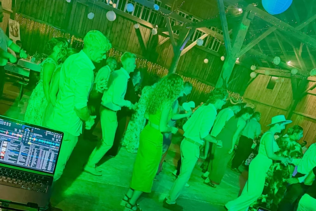 Tanzende Hochzeitsgäste in einer Holzscheune, DJ-Laptop im Vordergrund